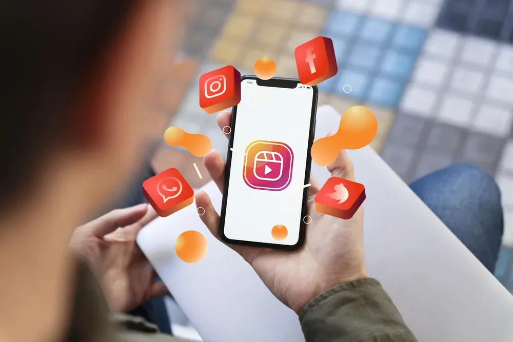 A phone with an Instagram icon on the screen and icons of social media portals around the phone.